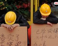 2012年12月25日，廣東中山，火炬開發(fā)區(qū)的多名建筑工人討要工作一年多的血汗錢一籌莫展，一些工人干脆將鋪蓋卷搬到了售樓部，并在門口搭起灶臺煮飯，希望以這種方式討回工錢。圖為在銷售中心門外，工人舉牌討薪。吳進(jìn)/視覺中國